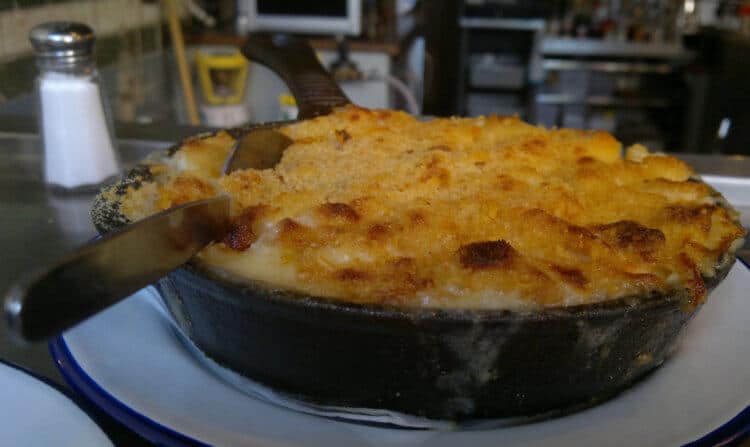A bowl of macaroni and cheese sits atop a restaurant plate